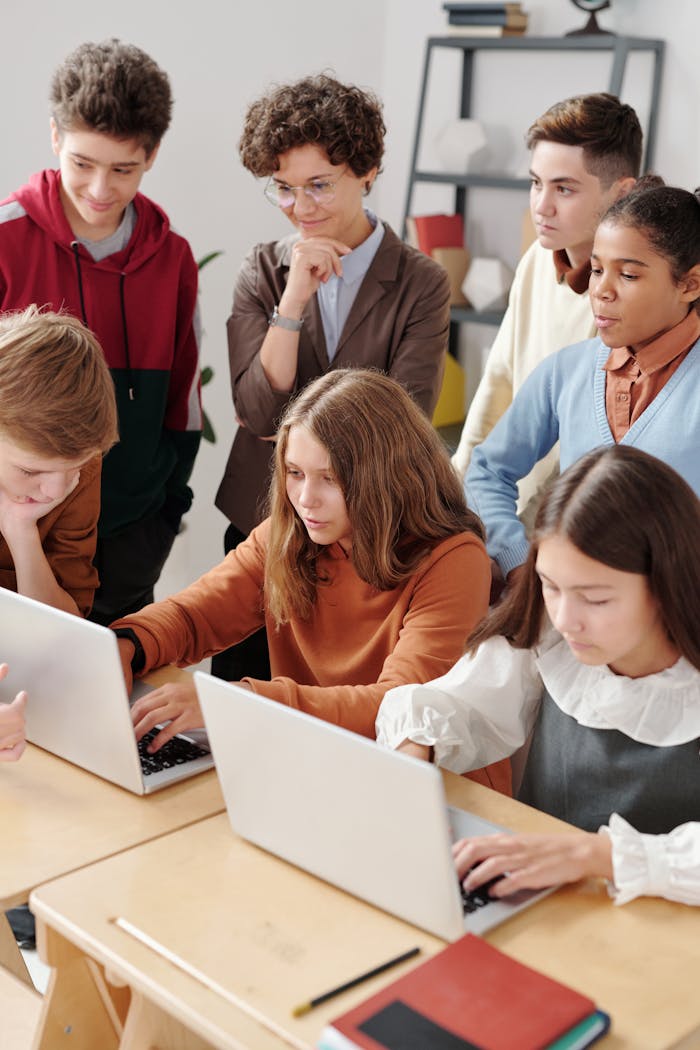 gallery-03 Group of teenagers in a classroom collaboratively working on laptops, fostering team learning.